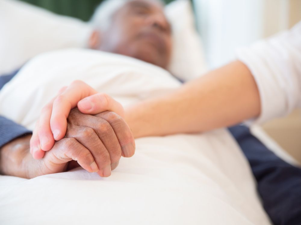 A hand gently holding the hand of someone resting in bed